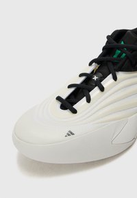 Scarpa da atletica bianca con lacci e dettagli neri. Presenta una parte superiore testurizzata con linee curve e un logo prominente sul lato. Design della suola liscia.