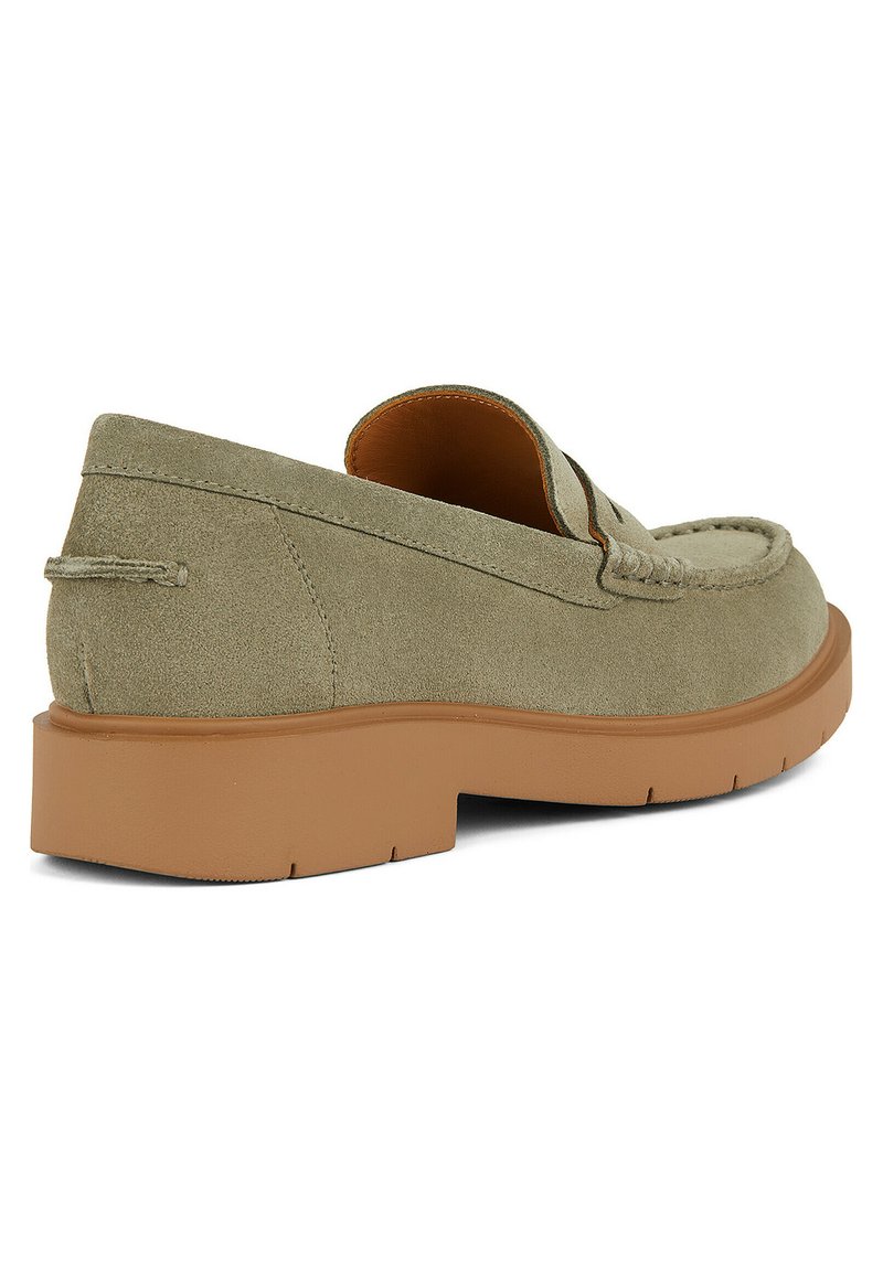 Mocassin en daim vert à enfiler avec un bout rond, semelle en caoutchouc marron contrastante et détails cousus sur le devant et le talon.