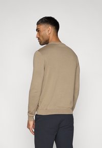 Μπεζ πλεκτό πουλόβερ με στρογγυλή λαιμόκοψη και μανσέτες με ριμπ ύφανση. Πλευρικά διακοσμητικά στοιχεία και λεπτή εφαρμογή. Εμφανίζεται η πίσω όψη.