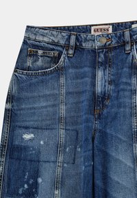 Denim-Jeans in einem mittleren Blauton mit einem verwaschenen Design, ausgestattet mit abgenutzten Flicken und Kupfernieten an den Taschen und am Bund.