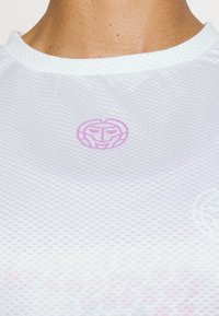 Biała sportowa koszulka z siateczki z okrągłym dekoltem, z subtelnym różowym logo umieszczonym na środku klatki piersiowej oraz teksturowanym wzorem materiału.