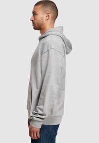 Sweat à capuche gris avec une coupe décontractée, grande poche avant et capuche réglable. Le tissu semble doux avec des poignets et un ourlet côtelés. Design décontracté.