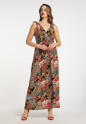 Vrouw met lang haar die een kleurrijke, patroonloze mouwloze maxi-jurk en bruine sandalen met hoge hakken draagt, staand op een witte achtergrond.