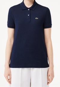 Polo bleu marine en tissu texturé, doté d'un col, de manches courtes et d'un petit logo vert sur la poitrine gauche.