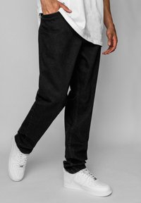 Sorte denimbukser med en afslappet pasform, der har sidelommer og diskrete syninger, parret med hvide sneakers.