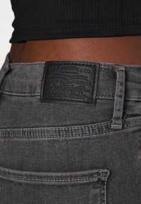 Grå denimjeans med ett strukturerat svart läderpatch som har präglat varumärke, sydda detaljer och en klassisk fickdesign.