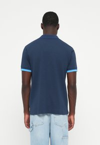 Marineblå polo t-shirt med korte ærmer, accentueret af lyseblå ribbede manchetter. Blødt stof, klassisk krave og ligeså lige kant.