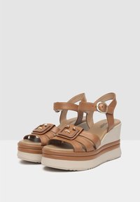 Sandali platform marroni con finitura in pelle liscia, cinturini larghi e dettagli in metallo su una spessa suola crema.