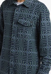 Fleece shirt met een geometrisch patroon in marineblauw, groen en lichtblauw, met een knoopsluiting en een borstzak.