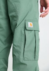 Pantalons cargo verts en tissu léger, dotés d'un motif en grille, de poches latérales et d'une étiquette carrée avec un logo orange.