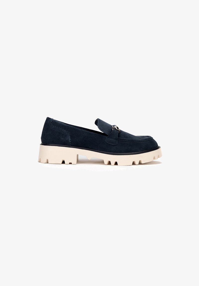 Mocasines de ante azul marino oscuro con suela beige gruesa, que cuentan con una tira frontal y acento de hardware metálico. Diseño simple y elegante con acabado texturizado.