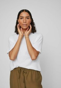 Tricou alb din bumbac cu mâneci scurte și croială lejeră, asortat cu pantaloni oliv cu șnur. Textură netedă, design simplu.