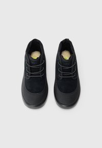 Une paire de chaussures UGG noires avec des lacets à l'avant, des embouts texturés et une doublure intérieure beige douce sur fond blanc uni.