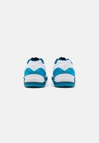 Des chaussures de sport blanches et turquoise. Elles présentent un talon rembourré, des semelles texturées et un matériau supérieur lisse avec un logo à l'arrière.