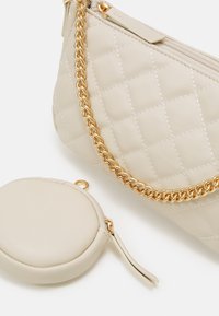Beige gesteppte Tasche aus Kunstleder mit goldener Kettenriemen und Reißverschluss. Enthält ein passendes rundes Münzfach mit einer Seitenschlaufe.