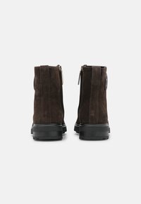 Botines de ante marrón con un acabado suave, que cuentan con una cremallera lateral y una gruesa suela de goma negra. Sin patrones ni acentos visibles.