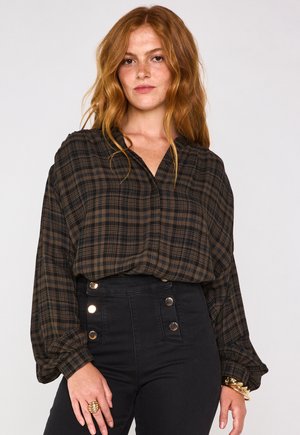 Chemisier à carreaux brun et noir, avec une coupe ample, un col en V et des manches longues, associé à un pantalon noir taille haute avec des boutons dorés.