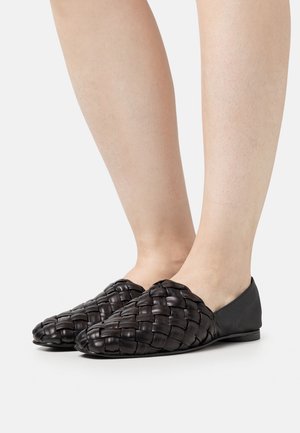 Scarpe slip-on in pelle intrecciata nera con suola piatta, caratterizzate da un motivo testurizzato a treccia e dettagli in pelle liscia sul tallone.