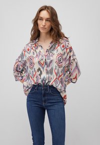 Long-sleeve, button-up shirt in a lightweight, patterned fabric featuring reds, purples, and blues. Paired with high-waisted denim jeans.