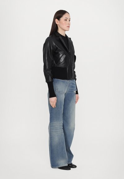 Black leather cropped jacket with side pockets, ribbed cuffs, worn over dark shirt and light blue wide-leg jeans with a faded texture.