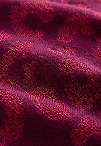 Gros plan sur un tissu bordeaux texturé avec un motif léopard en relief dans différentes nuances de rouge et de rose profond.