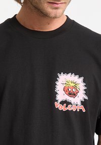 Una camiseta de algodón negra presenta un gráfico colorido con una cara ilustrada y la palabra "VOLCOM" en rojo, sobre un contorno blanco.