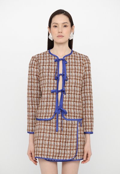 Textureret brunt og hvidt ternet blazer med blå trim, der har rund halsudskæring og dekorative snore fortil. Kort længde design.