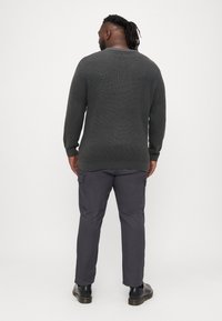 Tmavošedý pletený sveter s textúrovaným vzorom, skombinovaný s cargo nohavicami v zodpovedajúcej šedej farbe. Čierne čižmy dopĺňajú celý outfit.