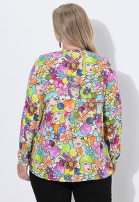 Blusa a maniche lunghe colorata con una stampa floreale e di volti in vivaci tonalità di rosa, verde, blu, arancione e giallo. Tessuto dalla texture morbida.