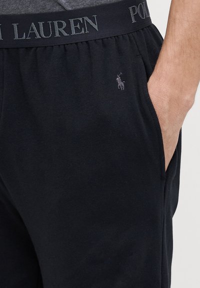 Crne trenirke s elastičnim pojasom i logotipom "Polo Ralph Lauren". Suptilni logotip izvezen na lijevom butinu. Glatka tekstura.