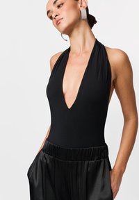 Fekete pánt nélküli body mély V-nyakkivágással, magas derekú fekete szatén nadrággal párosítva. Feltűnő csillogó fülbevalók és sima textúra.