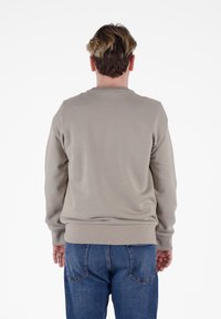 Felpa beige a girocollo con polsini e orlo a costine, caratterizzata da una texture morbida. Abbinata a jeans in denim blu con dettagli di cucitura.