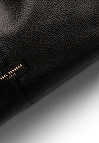 Schwarz strukturiertes Lederhandtasche mit rechteckiger Form und einem Etikett, das "ISABEL BERNARD PARIS" in goldener Schrift trägt.