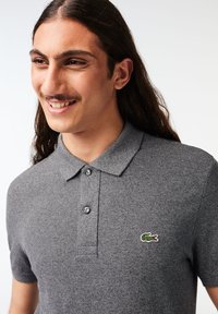 Camisa polo gris de tejido texturizado, con cuello y placket de tres botones. Incluye un pequeño logo verde y blanco en el pecho.