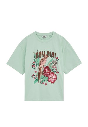 Camiseta de manga corta de color verde claro con un estampado tropical que incluye un loro, grandes flores rosas, hojas verdes y el texto "BOM DIA!" y "TROPICAL."