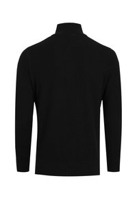 Sort sweater med et struktureret strikmønster, der har en høj krave og lange ærmer. Kanten nederst er ribstrikket for ekstra detaljer og struktur.