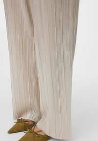 Pantalons plissés crème avec un design texturé, présentant une jambe large et un léger éclat. Associés à des ballerines pointues vert olive.