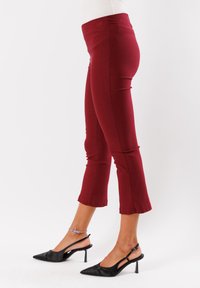 Pantaloni cropped bordeaux con vita aderente, texture liscia e fondo a campana. Abbinati a décolleté nere con punta a punta.
