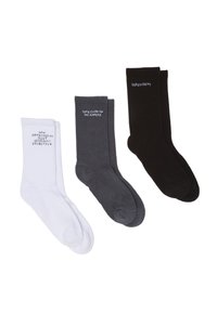 Drei Paar Knöchelsocken: weiß, grau und schwarz, mit kontrastierenden Textdrucken. Der Stoff wirkt weich und hat eine gerippte Textur.