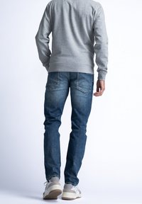 Pánská šedá mikina, modré džínové kalhoty a světlé šedé tenisky. Džíny mají klasický střih, s viditelnými zadními kapsami a decentním vyblednutím.