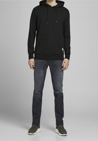 Czarna bluza z kapturem z przednią kieszenią, ściągaczami oraz troczkami, zestawiona z ciemnymi dżinsami i brązowymi trampkami. Prosty, funkcjonalny design.