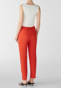 Pantalons taperred rouges avec une taille élastique et deux poches arrière, associés à un haut blanc sans manches ajusté. Tissu lisse, design minimal.