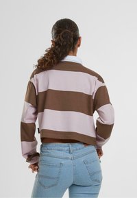 Brun og lys rosa stripete hettegenser, kort design, lange ermer, med rund hals. Kombinert med blå denimjeans.