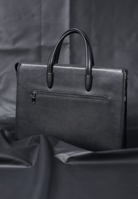 Sort lædermappe med en struktureret overflade, der har to håndtag i toppen og en frontlomme med lynlås. Glat samlet finish.