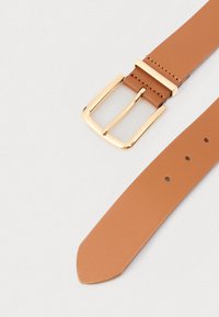 Correia de relógio em couro castanho com fivela metálica dourada. Apresenta textura suave, extremidade pontiaguda e vários furos para ajuste.