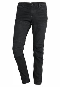 Musta denimpöytä, jossa on kapea istuvuus, vahvistetut polvipaikat ja klassinen viiden taskun muotoilu, jossa on edessä nappi- ja vetoketjukiinnitys.