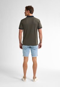 Pruhovaná polo košile v olivové a námořnické barvě s krátkými rukávy, spárovaná se světle modrými džíny. Obuv tvoří béžové tenisky s kontrastní patou.