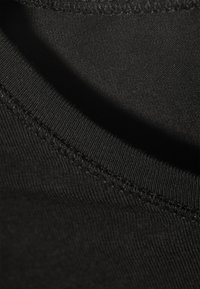 Zbliżenie czarnego materiału ukazujące szczegółowe przeszycia i teksturę ryfrowego dekoltu.