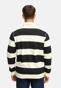 Pullover a righe nero e crema con colletto, maniche lunghe e polsini a coste. Presenta cuciture a contrasto lungo l'orlo.