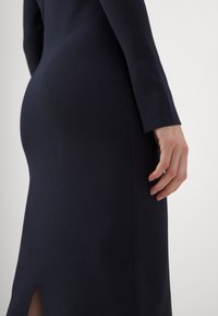 Robe en tricot marine à manches longues et fente latérale, présentant une silhouette près du corps et une texture lisse, mettant en avant des lignes épurées et un design minimal.